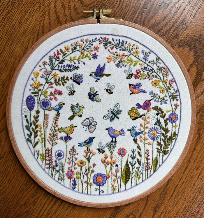 Vibrant embroidery creations depicting a circle of flowers, birds, butterflies, and bees, great for an embroidery hobby.