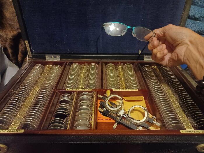 Optical lens kit held by hand with glasses above, showcasing redneck engineering in an inventive setup.