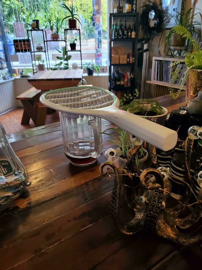 A blender with a tennis racket attached, showcasing redneck engineering creativity on a wooden table in a cozy room.