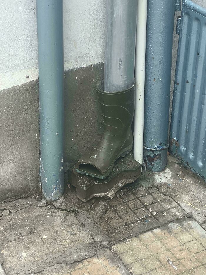 Green rubber boot used as a makeshift holder for a drainpipe on a rough concrete base, an example of redneck engineering.