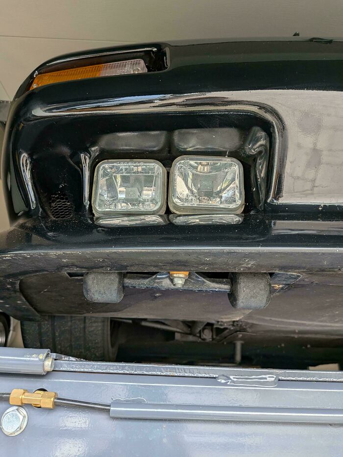 Close-up of makeshift car fog lights revealing redneck engineering modifications on vehicle front end components.