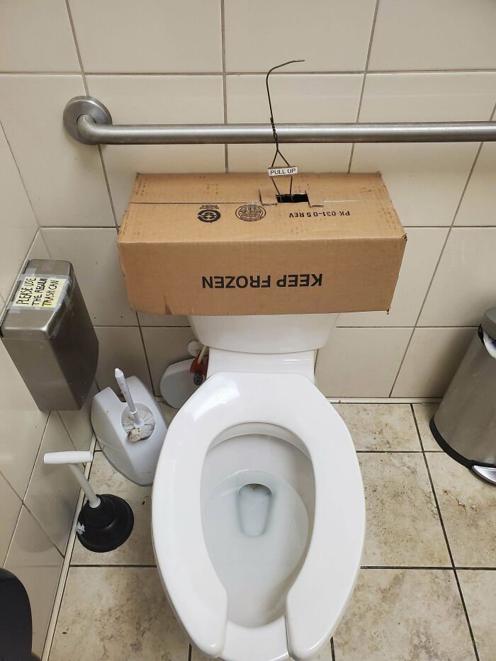 Toilet with a cardboard box labeled keep frozen and a wire pull-up handle shows a redneck engineering bathroom fix.