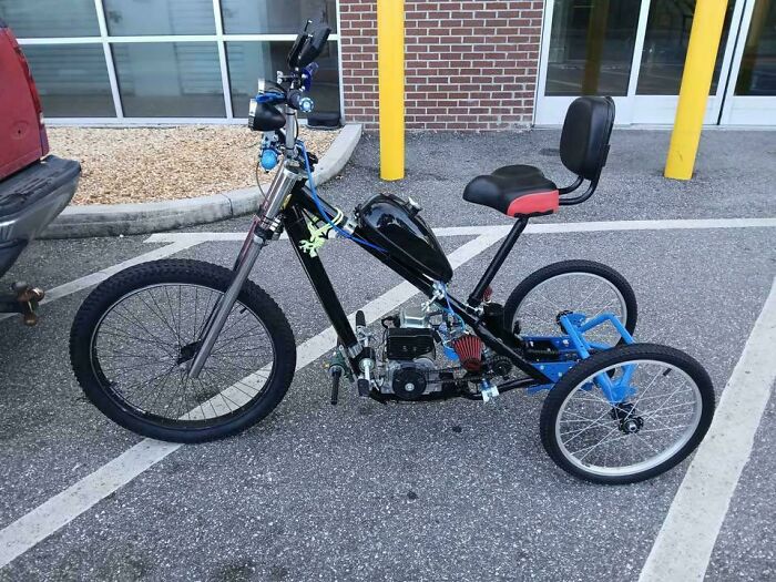 Homemade motorized tricycle with custom redneck engineering modifications parked in a lot next to a building.