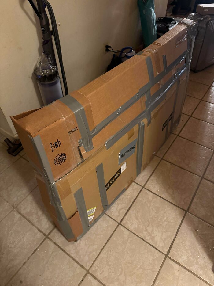 Cardboard box reinforced with excessive duct tape on tiled floor, an example of redneck engineering craftsmanship.