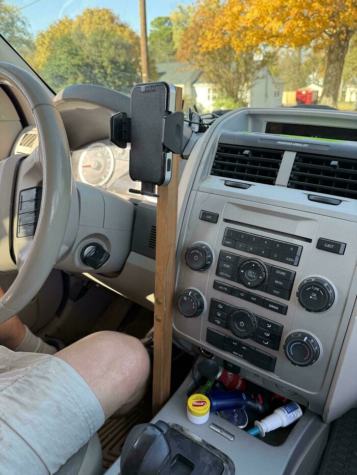 Car interior showing redneck engineering with a wooden phone holder mounted next to the steering wheel.