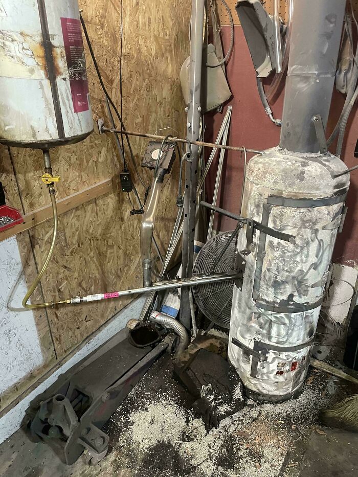 Improvised redneck engineering setup with old water heater and makeshift piping in a cluttered workshop corner.