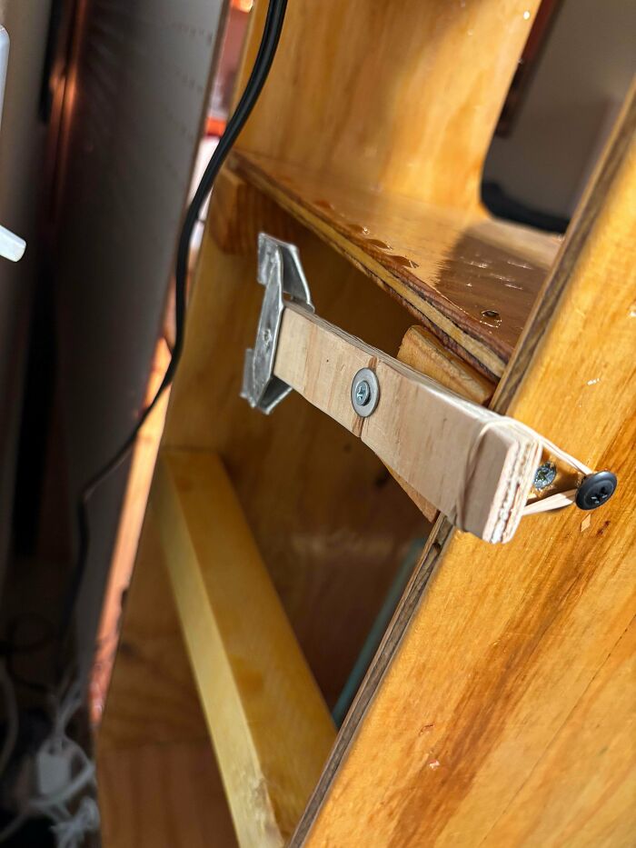 Improvised wooden bracket with metal hinges holding a panel, an example of redneck engineering in a home setting.