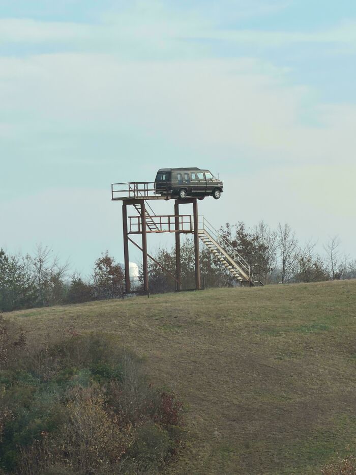 Van parked on a high platform with stairs in a rural area, an example of redneck engineering outdoors.