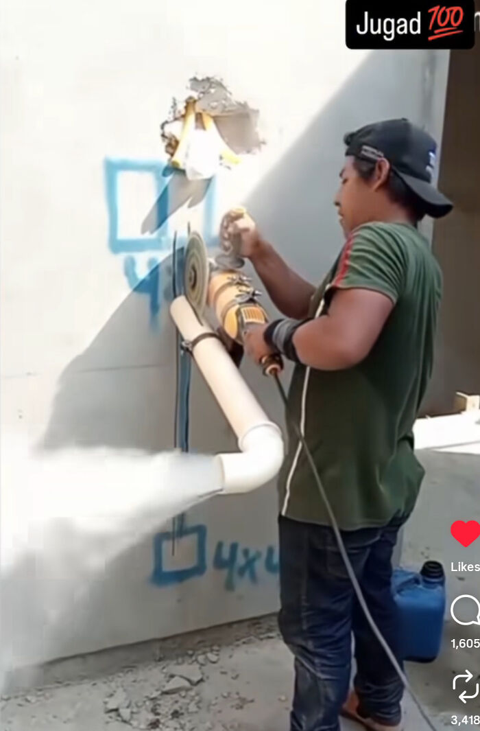 Man using redneck engineering with a grinder attached to PVC pipe that emits smoke against a concrete wall outdoors.