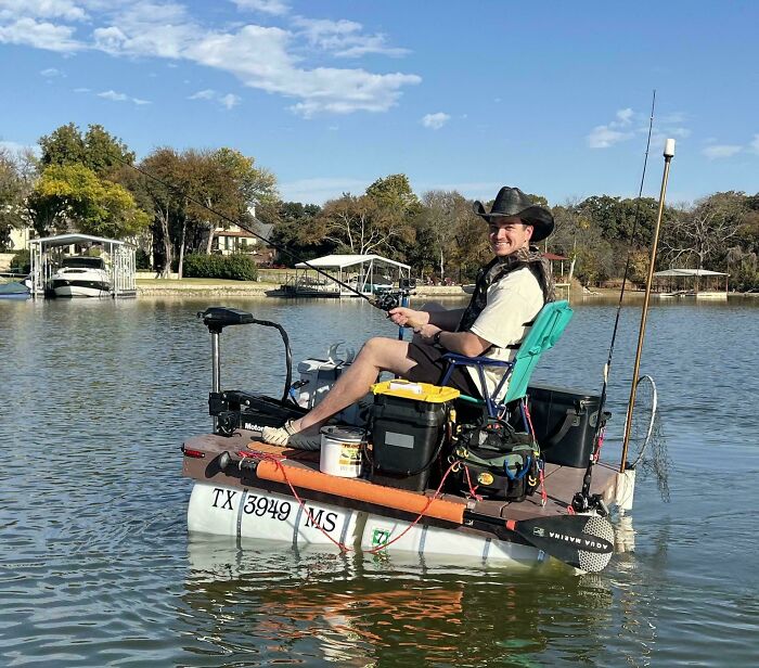 Man fishing on a homemade floating platform with DIY equipment, showcasing redneck engineering on a calm lake.