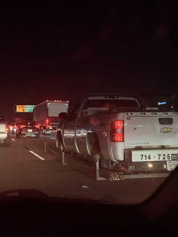 Pickup truck carrying long metal rods with an unconventional setup, an example of redneck engineering on a highway at night.