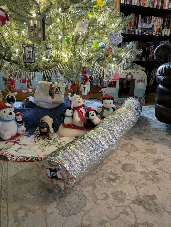 Flexible ventilation duct placed under decorated Christmas tree with holiday plush toys, a clear example of redneck engineering.