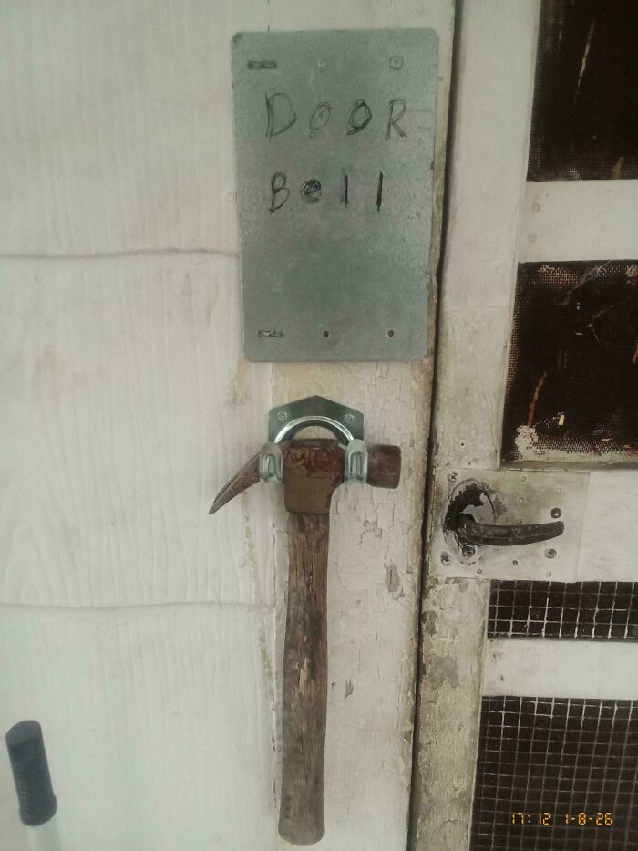 Improvised redneck engineering doorbell using a hammer fixed to the wall with metal brackets and handwritten sign.