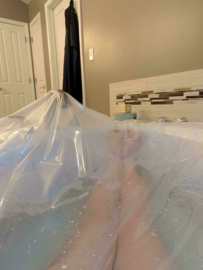 Feet covered in clear plastic in a bathtub, an example of redneck engineering in a home bathroom setting.