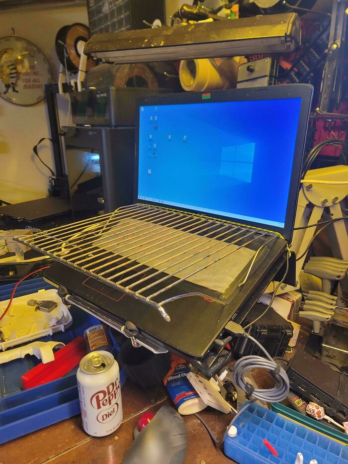 Laptop with a metal grill placed on keyboard in a cluttered workspace showing an example of redneck engineering.