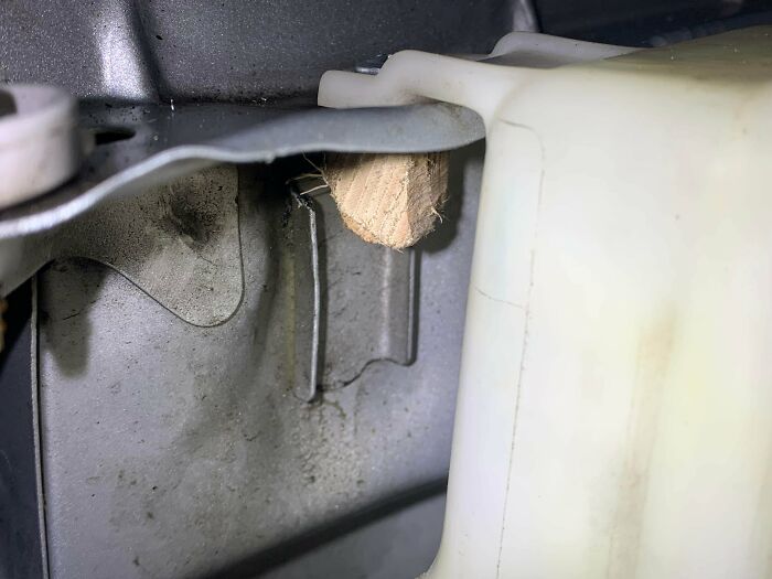 Close-up of redneck engineering using a wood wedge to secure a metal car part inside the engine compartment.