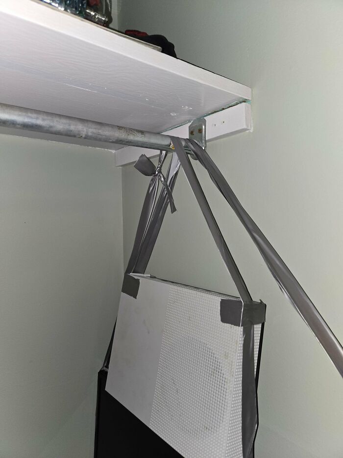 Improvised redneck engineering solution using duct tape to hang a gaming console on a closet rod, risking damage.
