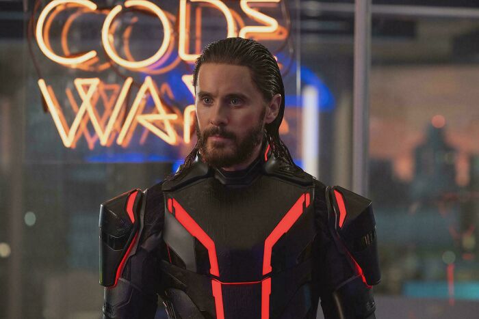 Actor in futuristic armor with red lights, standing in front of neon sign, illustrating absurd movie and TV details.