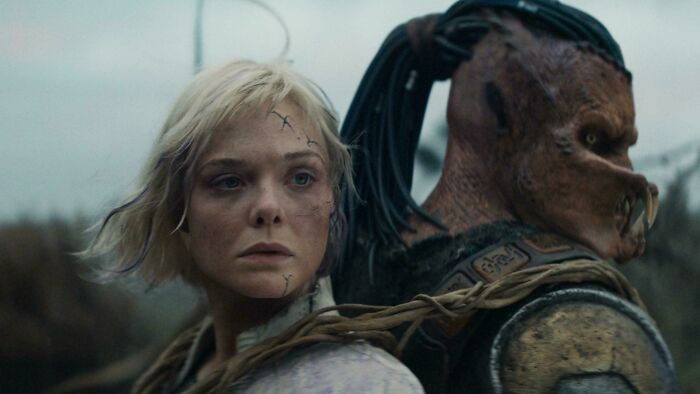 Blonde woman with scars stands back to back with a creature in armor, showcasing absurd movie and TV details.