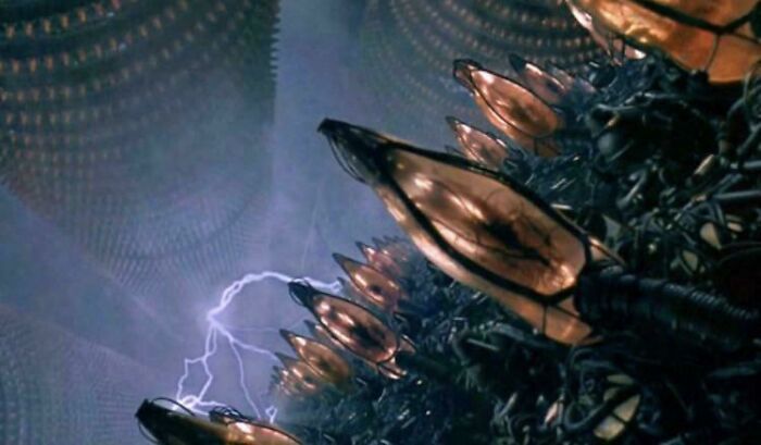 Scene from a sci-fi movie featuring large mechanical devices with lights and a bolt of lightning inside a futuristic chamber.