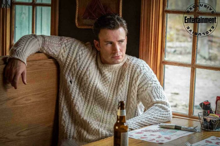 Actor in a cozy sweater sitting by a diner window with a beer bottle, illustrating absurd movie and TV details.
