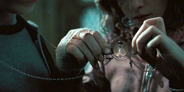 Close-up of two people holding a vintage pocket watch, highlighting absurd movie and TV details in a dim setting.