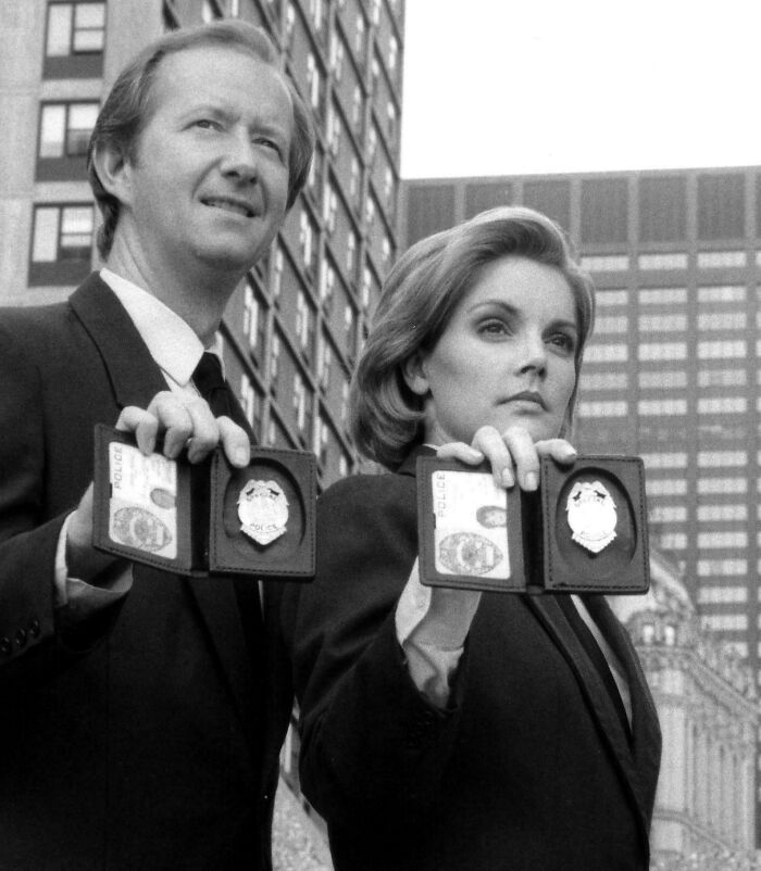 Two detectives holding up police badges in a black and white ’90s scene, evoking childhood memories and nostalgia.