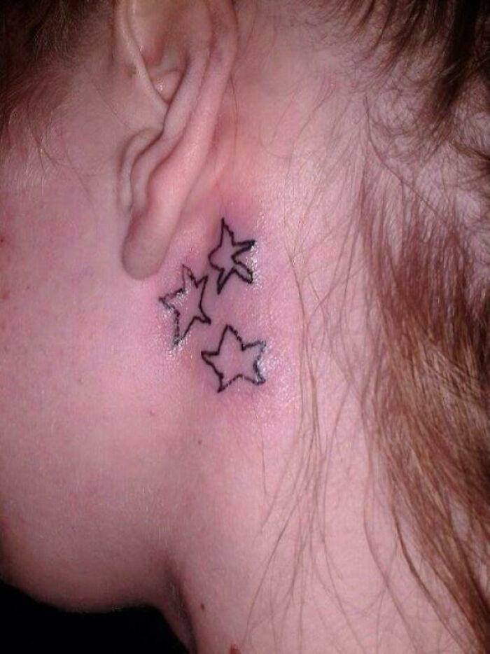 Close-up of a poorly done star tattoo behind the ear, showing a bad tattoo design with uneven lines and shapes.