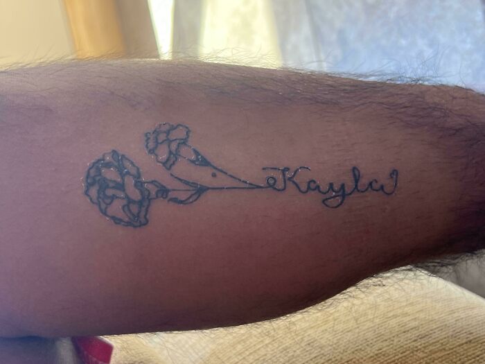 Tattoo of a misspelled name with poorly drawn flowers on an arm, showcasing a bad tattoo example.