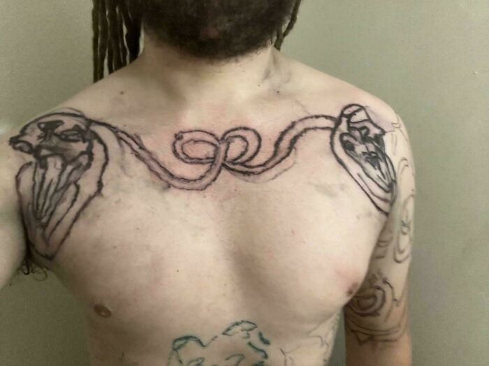 Man showing a chest tattoo with two heart outlines connected by a crude rope design, a bad tattoo example.