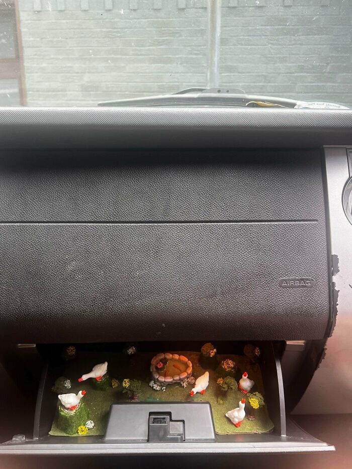 Car glove compartment converted into a DIY miniature garden scene with small chickens and greenery inside.