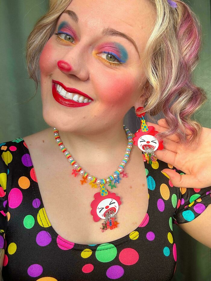 Smiling person with colorful clown makeup, wearing DIY handmade rainbow necklace and matching earrings in polka dot outfit.