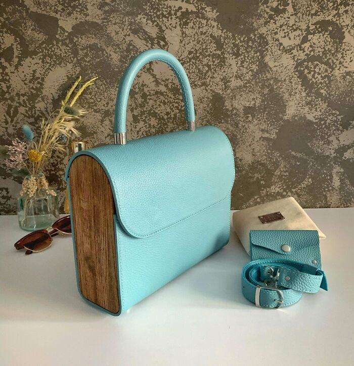 Blue leather DIY handbag with wooden sides, matching belt and pouch, styled on white surface with dried flowers nearby.