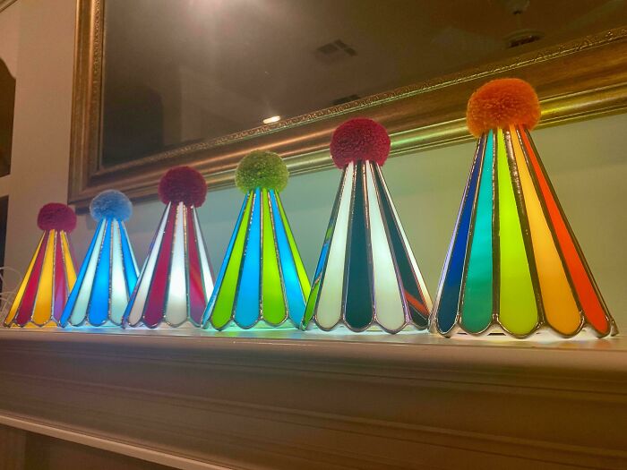 Colorful DIY stained glass cone decorations with pom-poms on top, displayed on a mantelpiece as a creative home project.