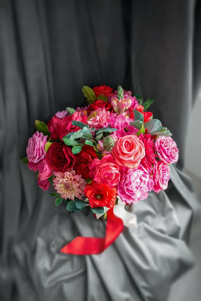 Colorful DIY flower bouquet with pink and red roses and green leaves, styled against a gray fabric backdrop.