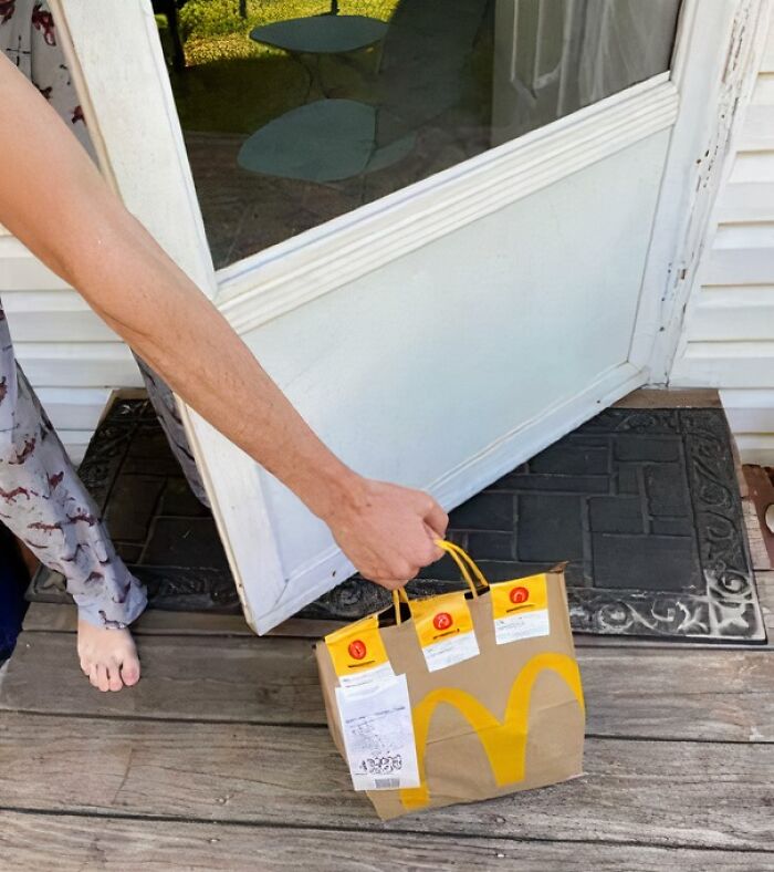 Person picking up a McDonald's delivery bag from a doorstep as part of hilarious delivery confirmation pics sent to customers.