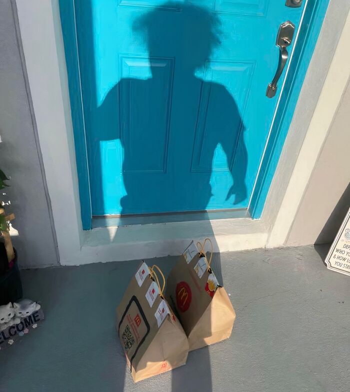 Shadow of delivery driver on bright blue door with two McDonald's paper bags on doorstep as delivery confirmation pic