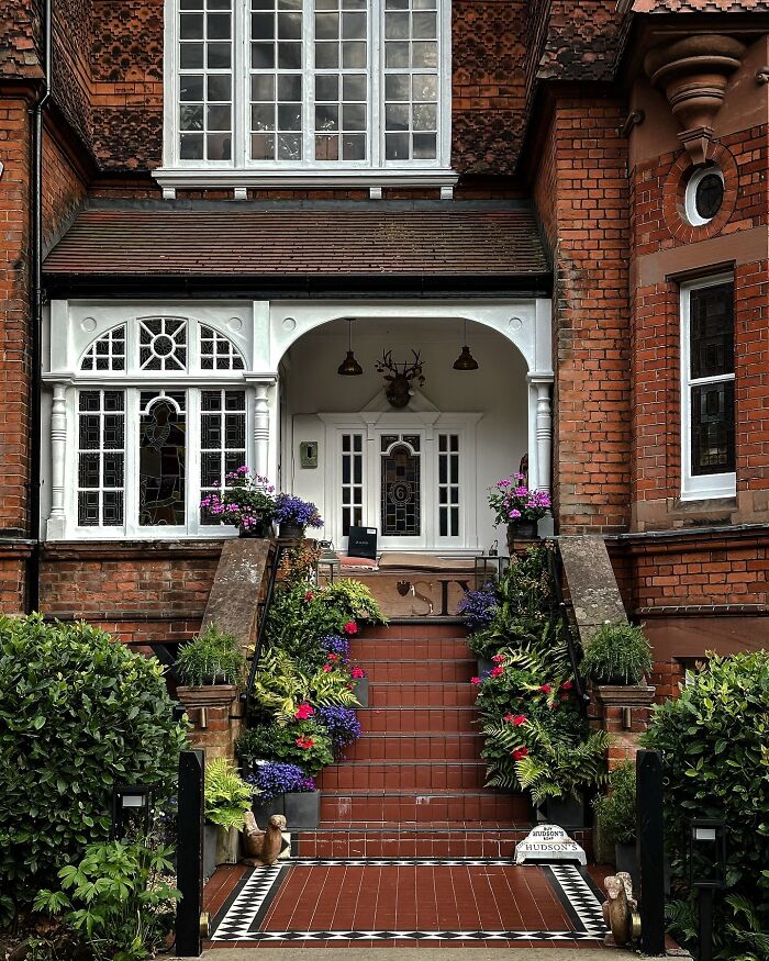 The front entrance of a brick house with beautiful architecture, a welcoming porch, and vibrant potted plants.
