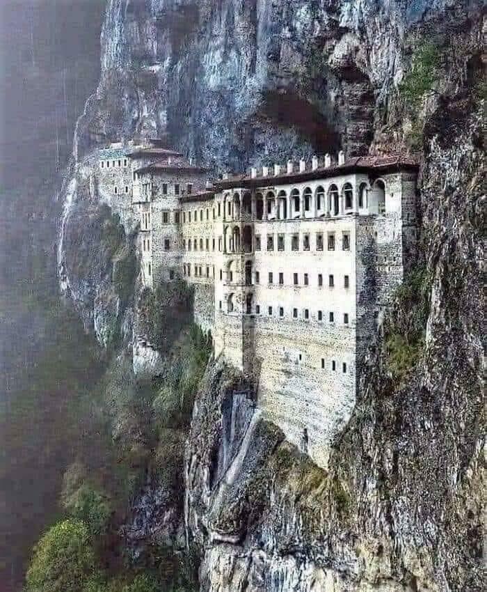 An ancient monastery with beautiful architecture built into the side of a steep, misty mountain.