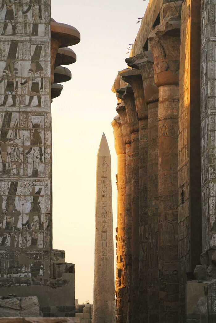 Ancient Egyptian architecture featuring towering carved columns and an obelisk against a bright sky.