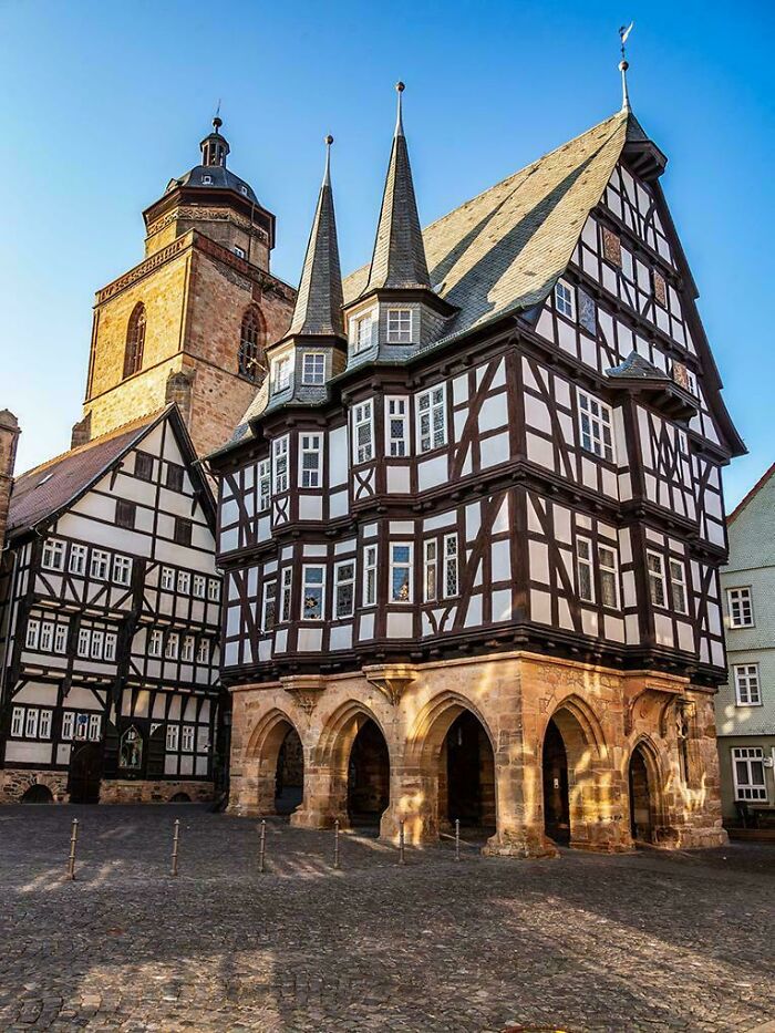 Historic timber-frame architecture with intricate details, arched entrance, and a church tower in the background.