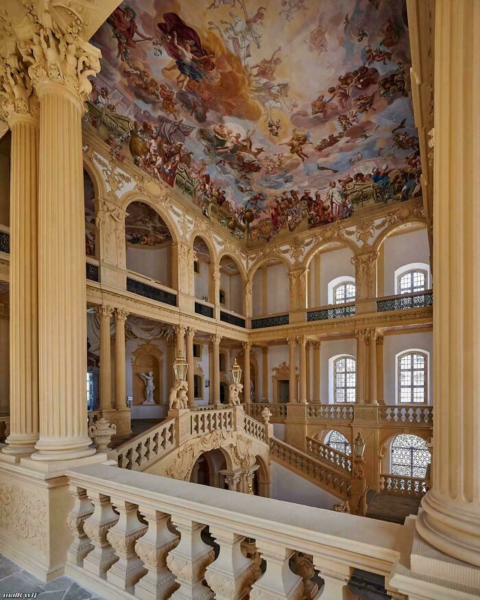 Opulent Baroque architecture with a grand staircase, columns, and a beautifully painted ceiling.