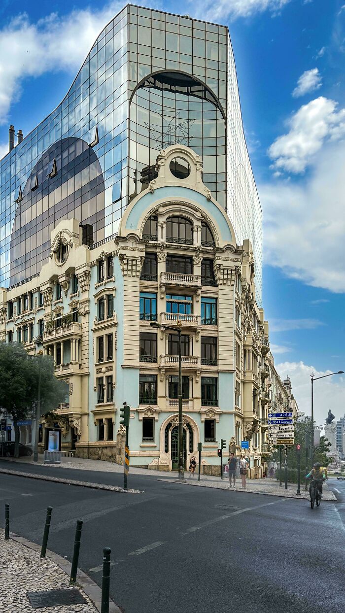 A blend of old and new architecture, with a classic building in the foreground and a modern glass skyscraper behind.