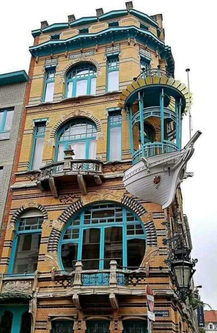 Unique architecture with a ship's bow protruding from a building, featuring ornate details and bright blue windows.