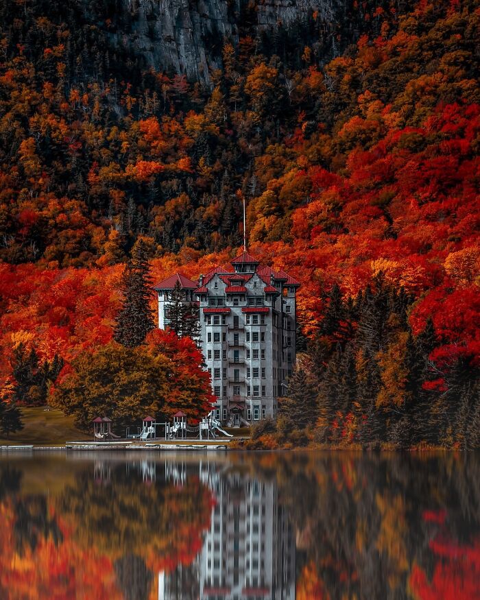 Stunning architecture of a grand building surrounded by vibrant autumn foliage, reflected in a still lake.