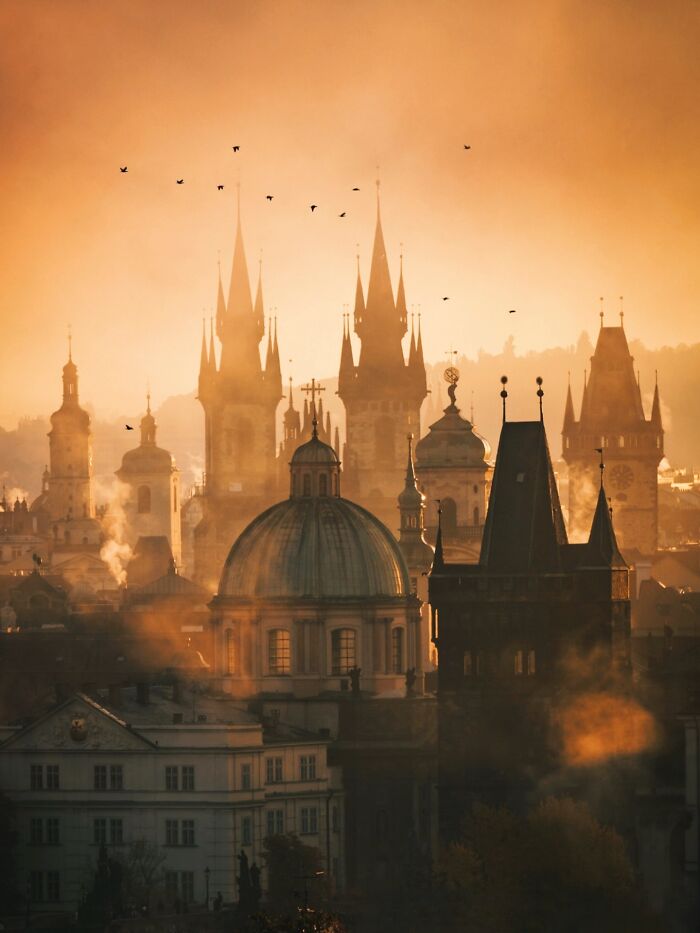Misty sunrise over Prague skyline, highlighting the beautiful architecture of historic spires and domes.