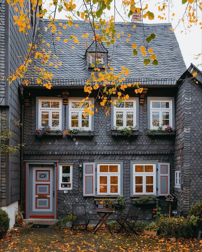 Quaint German architecture with dark shingle siding, white windows, and yellow autumn leaves.