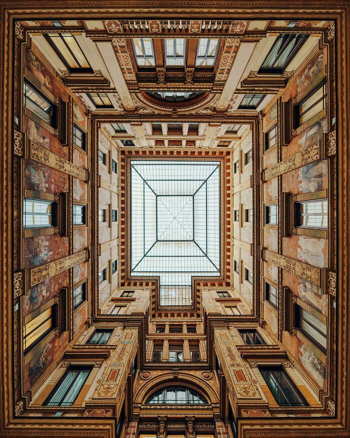 Looking up at symmetrical architecture of a building's inner courtyard with a large glass ceiling.