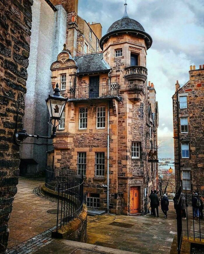 Charming old stone building with a circular tower and narrow street, showcasing unique architecture.