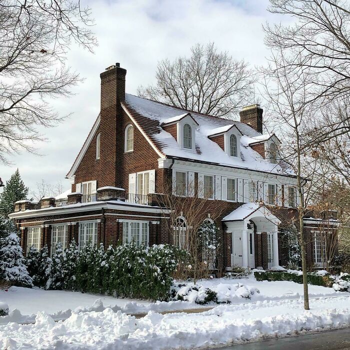 Beautiful architecture of a classic brick house covered in snow, with white shutters and dormer windows.